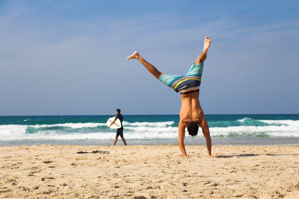 man doing handstand on beach